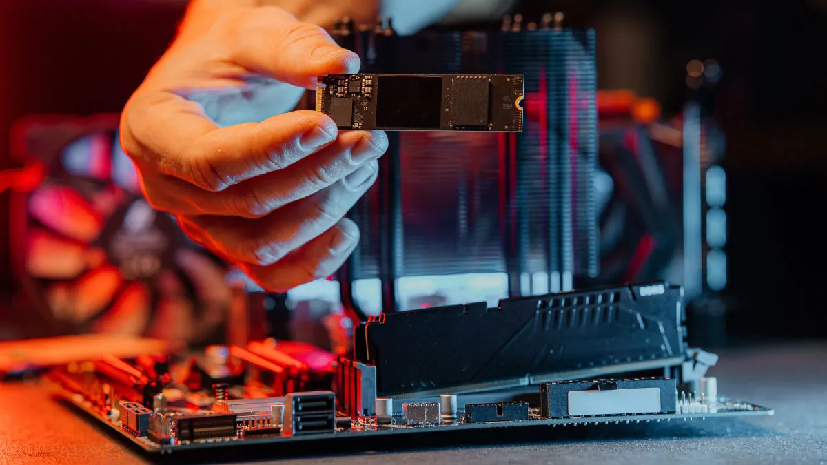 Eine Hand hält eine M.2-SSD über ein Mainboard.