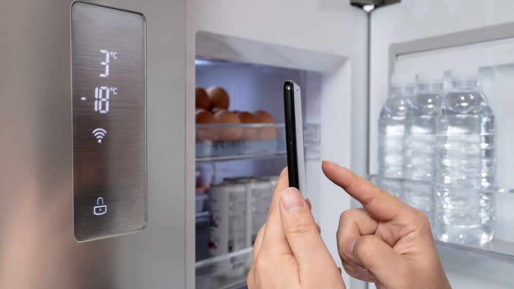 Eine Person steuert den Kühlschrank mithilfe des Smartphone in ihrer Hand.