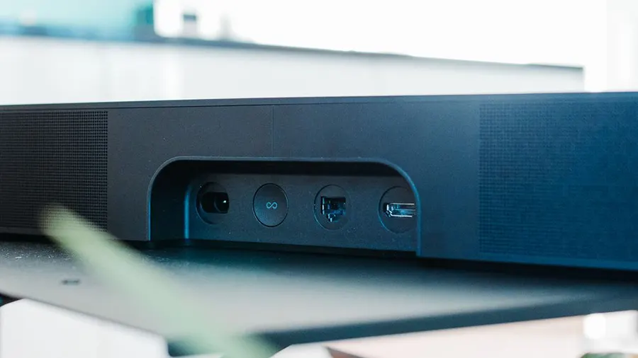 Eine dunkle Soundbar mit Anschlüssen für Strom, Netzwerk und USB auf einem Tisch vor einem verschwommenen Hintergrund.