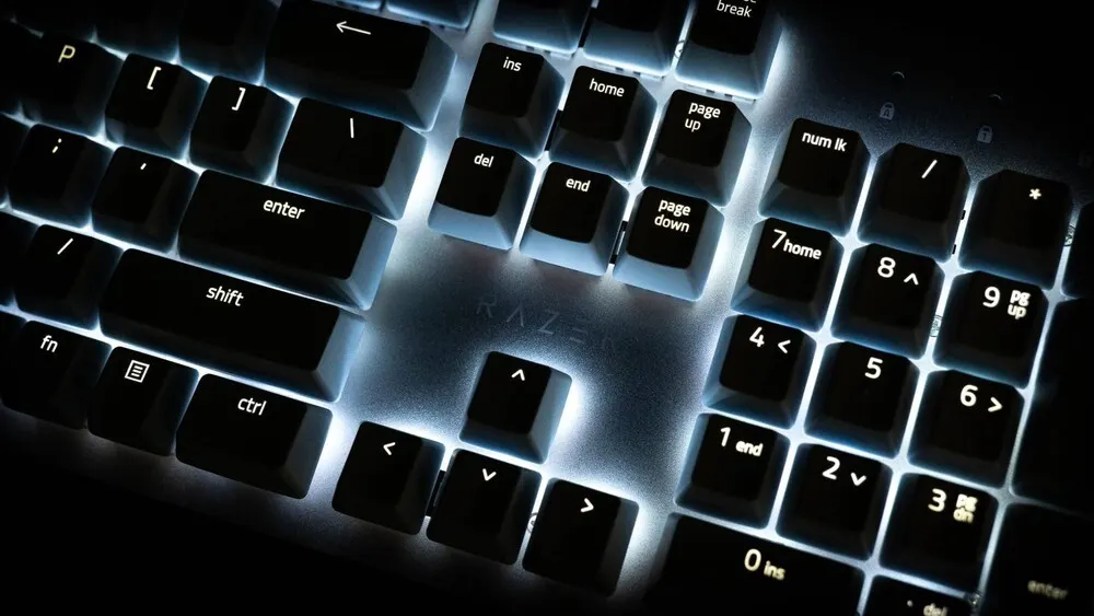 Nahaufnahme einer Computertastatur mit Hintergrundbeleuchtung unter schwachem Licht. Tasten mit Beschriftungen wie "Enter", "Shift" und Zahlen sind sichtbar.
