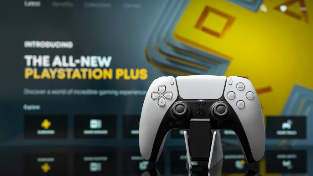 Ein weißer PlayStation 5 Controller steht auf einer schwarzen Ladestation vor einem Bildschirm. Der Bildschirm zeigt Text und Icons.