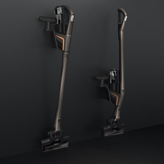 Zwei dunkle, kabellose Staubsauger sind an einer Wandhalterung befestigt. Sie haben orangefarbene Akzente.