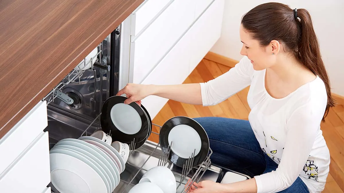 Frau räumt Teller mit schwarzem Rand in eine geöffnete Spülmaschine.