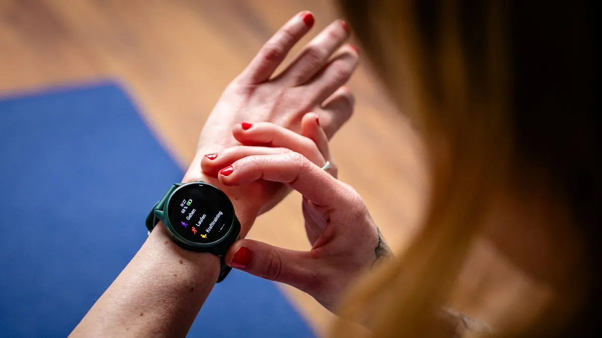 Nahaufnahme einer Person, die eine grüne Smartwatch mit Trainingsoptionen am Handgelenk trägt.