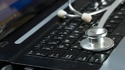 Ein schwarzer Laptop mit einer Tastatur, auf der ein silbernes Stethoskop liegt.