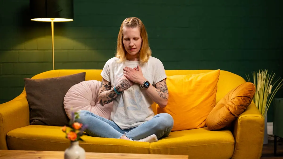 Franzi sitzt im Schneidersitz auf dem Sofa und hält ihre Hände über ihr Herz.