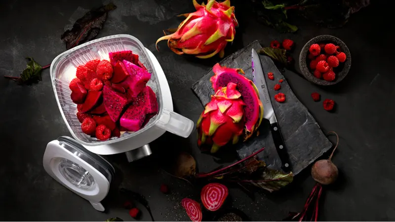 Auf einem dunklen Tisch liegen Drachenfrüchte, Himbeeren, Rote Bete, ein Messer und ein Mixerbehälter.