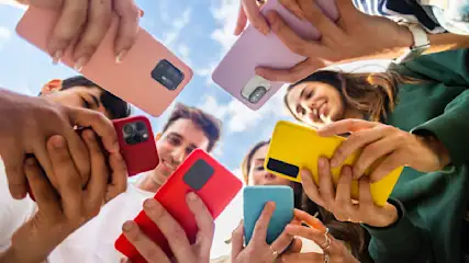 Eine Gruppe von Menschen hält Smartphones in bunten Hüllen vor einem Himmel mit Wolken.