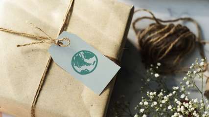 Ein Geschenk in dunkles motivloses Papier eingepackt. An der Schleife aus Bio-Material hängt ein Schild mit einem grünen Welt Symbolzeichen.
