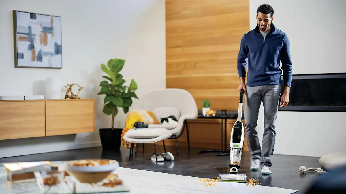 Ein Mann saugt im Wohnzimmer große Krümel mit dem Bissell CrossWave X7 Plus Cordless Pet Select Wischsauger auf.