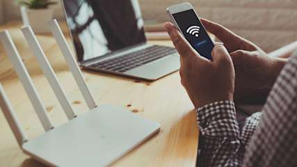 Arme eines Mannes, der ein Smartphone hält und vor einem Router sitzt