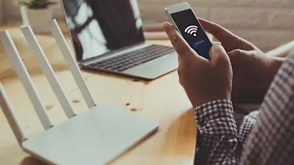 Arme eines Mannes, der ein Smartphone hält und vor einem Router sitzt