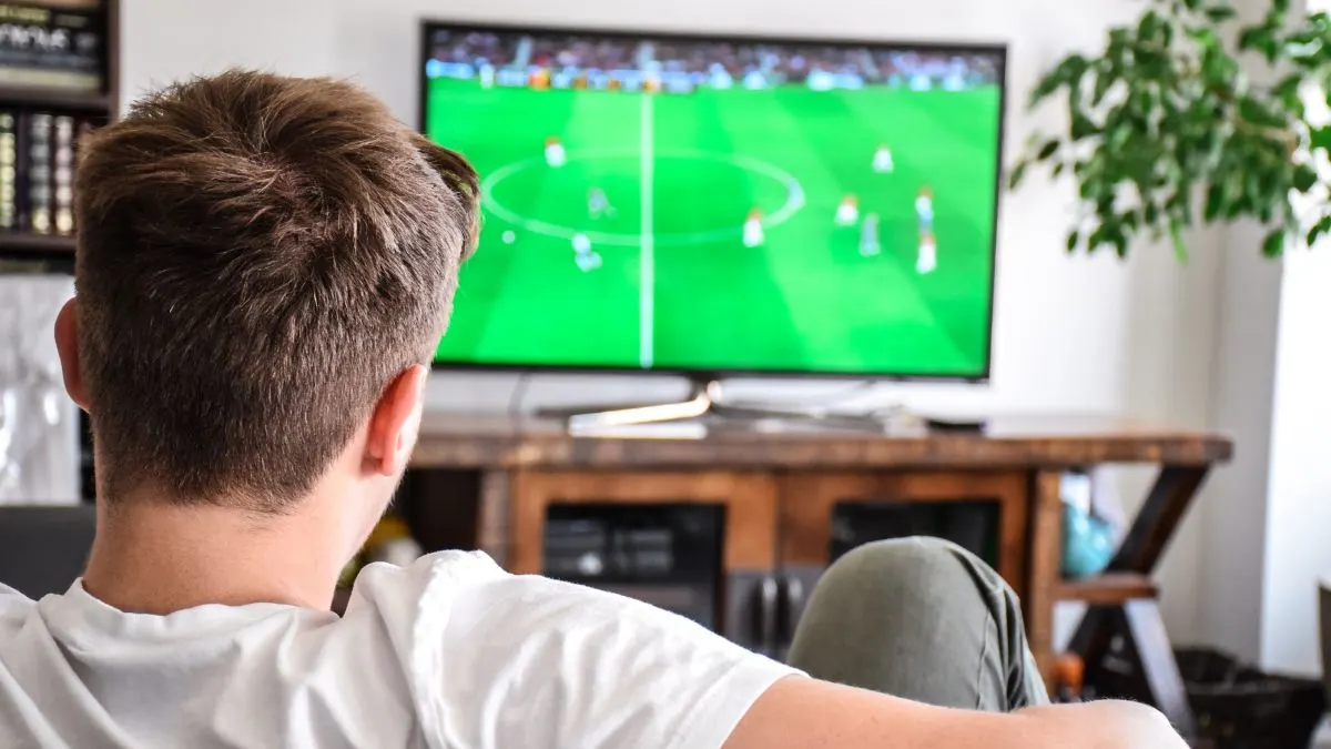 Ein junger Mann sieht sich ein Fußballspiel im Fernsehen an.
