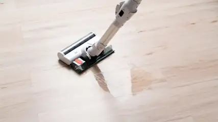 Ein weißer Staubsauger mit einem schwarzen und roten Detail steht auf einem hellen Holzboden.