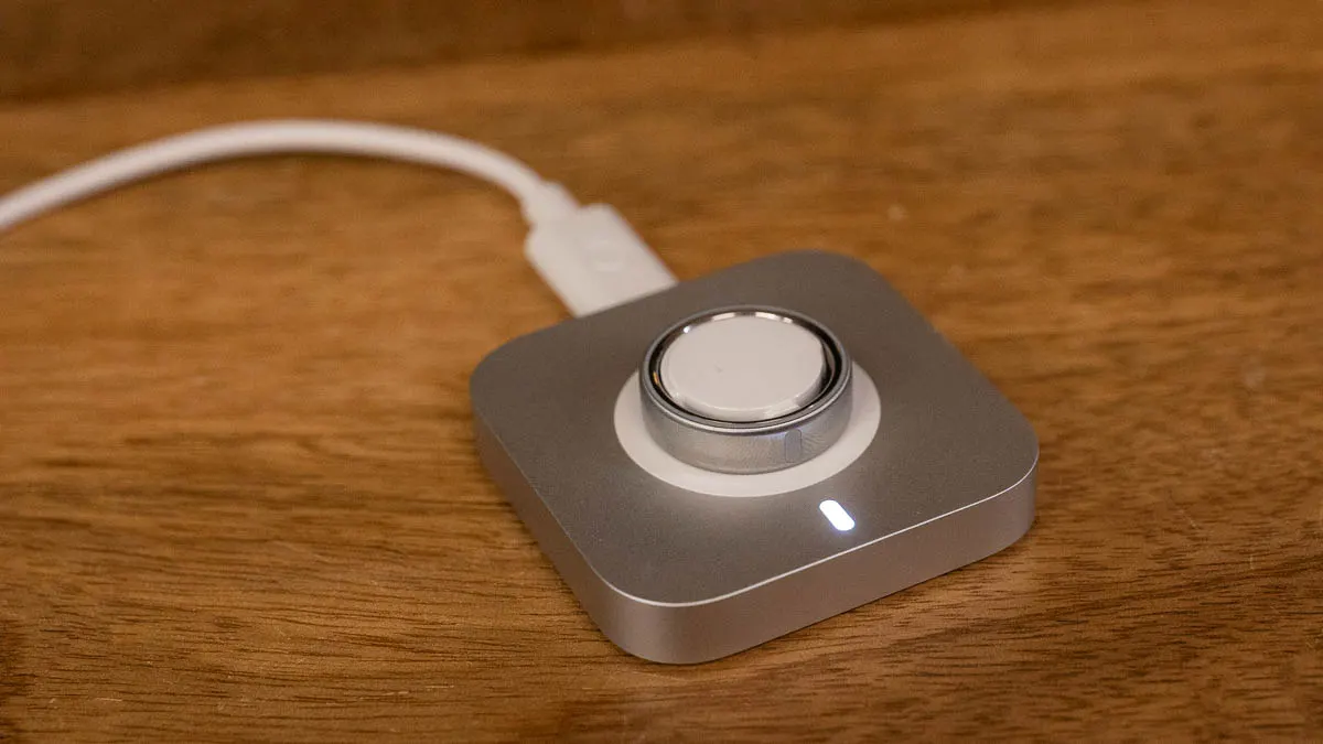 Der Oura Ring 5 liegt auf der Ladestation, eine weiße LED zeigt an, dass er lädt.