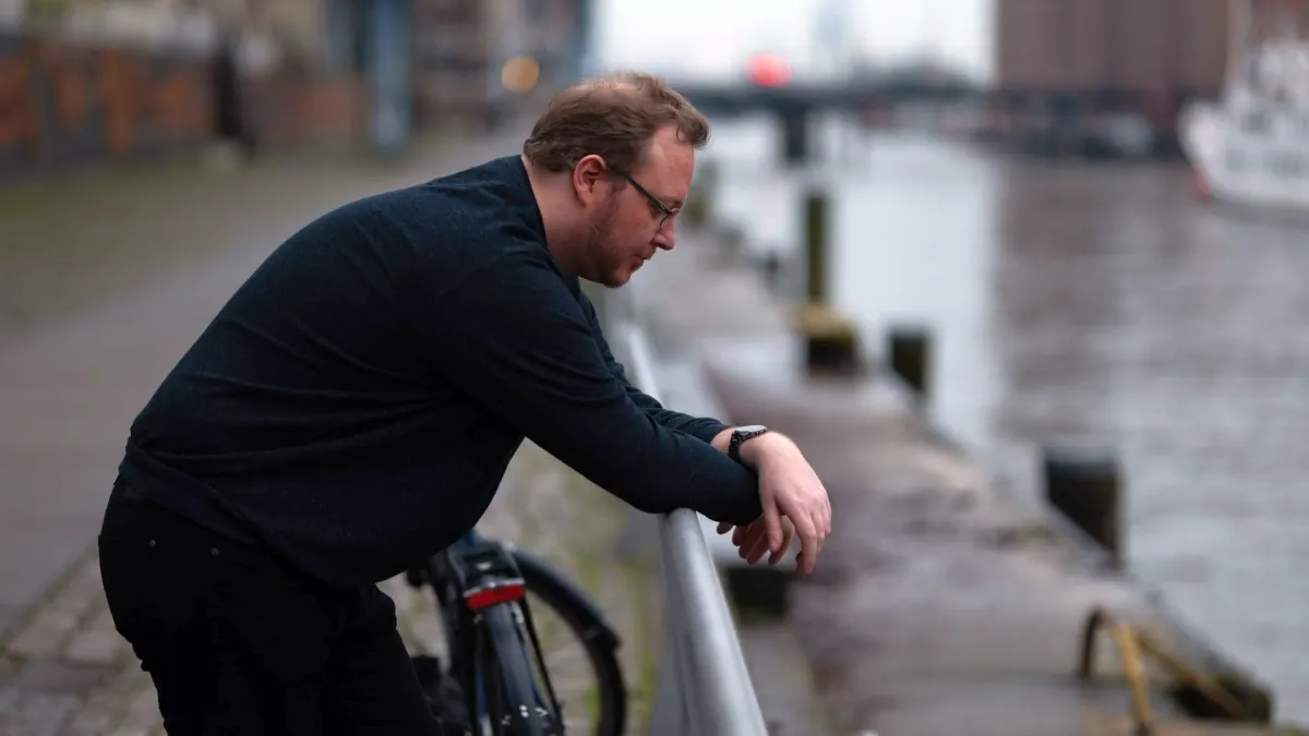Andreas lehnt am Hamburger Hafen an einem Geländer und schaut auf seine Smartwatch.