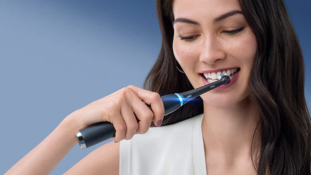 Eine Frau putzt ihre Zähne mit einer elektrischen Zahnbürste von Oral-B.