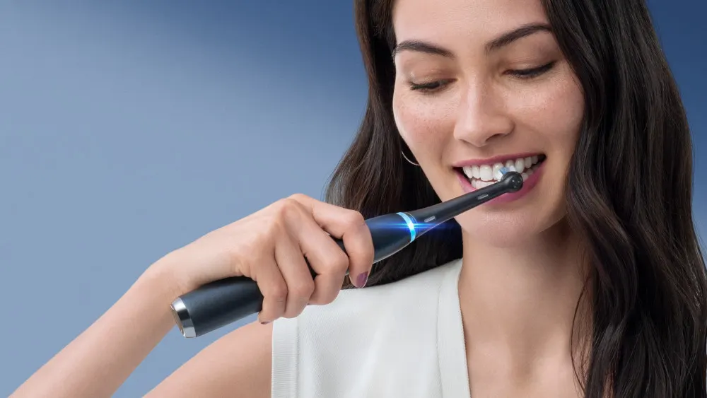 Eine Person putzt Zähne mit einer elektrischen Zahnbürste vor einem blauen Hintergrund.