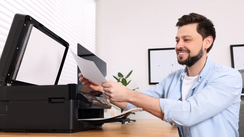 Ein Mann nutzt einen Drucker und sicht sich den Ausdruck an.