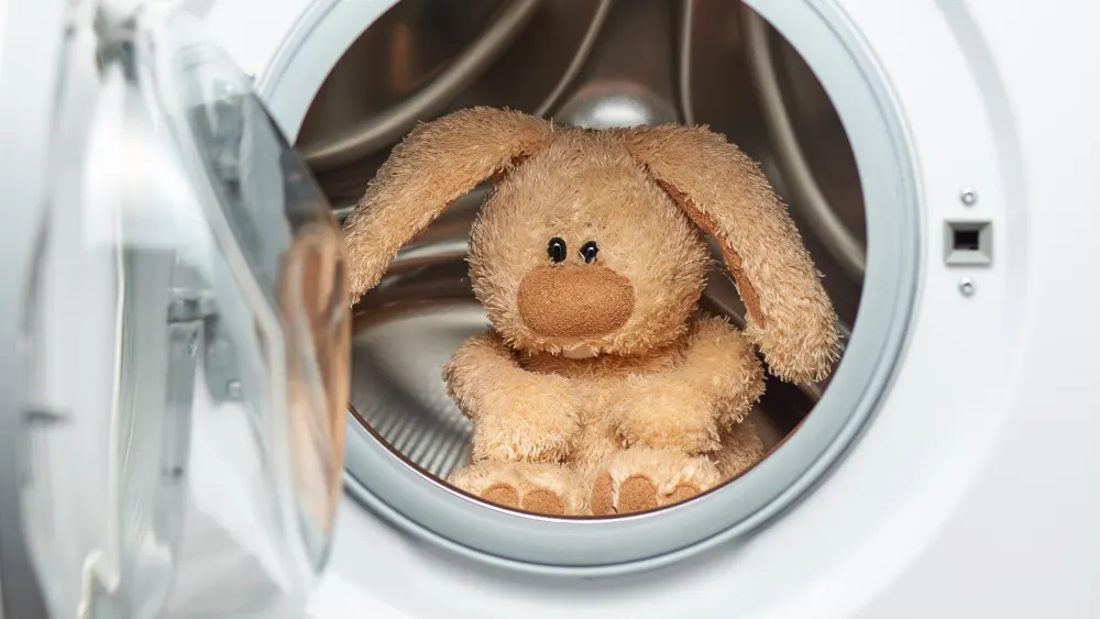 Ein Stoffhase mit langen Ohren sitzt in einer weißen Waschmaschine mit einer teilweise geöffneten Tür.