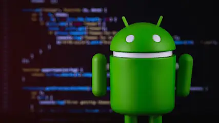 Ein grüner Android-Roboter steht vor einem dunklen Bildschirm mit Codezeilen. Das Licht betont die Form des Roboters.