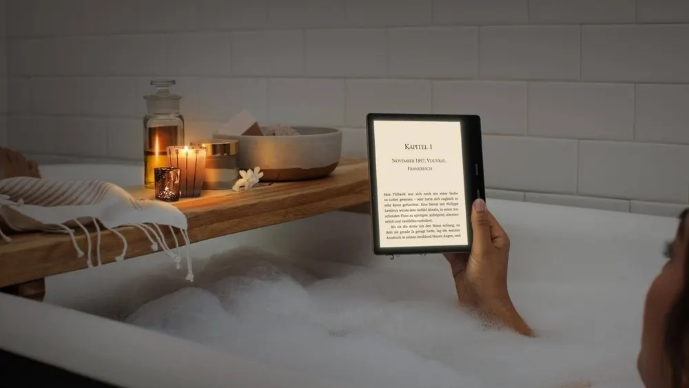Eine Person liest in einer Badewanne ein E-Book. Kerzen und eine Schale stehen auf einer Holzablage über der Wanne.