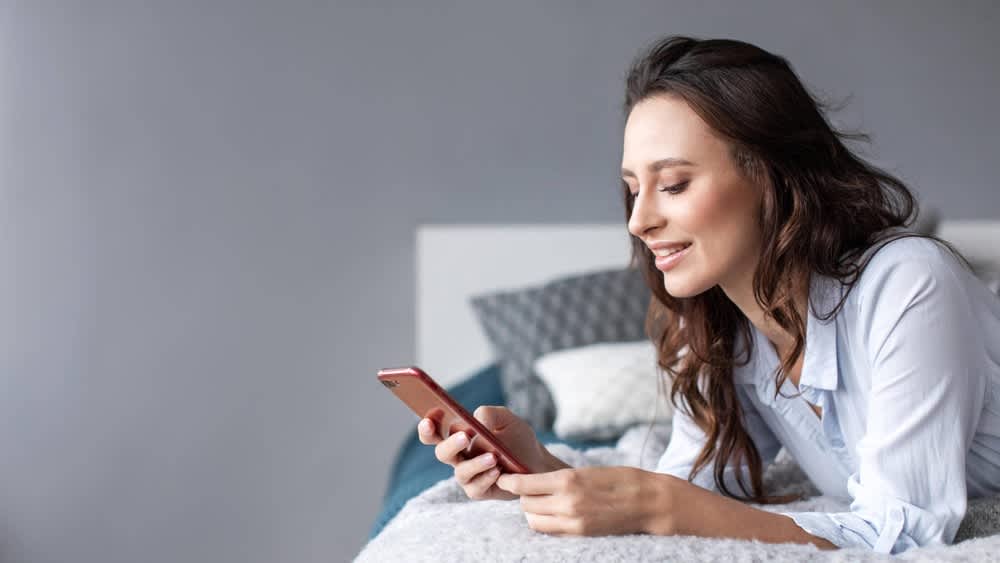Eine Frau liegt mit einem Smartphone in der Hand auf einem Bett.