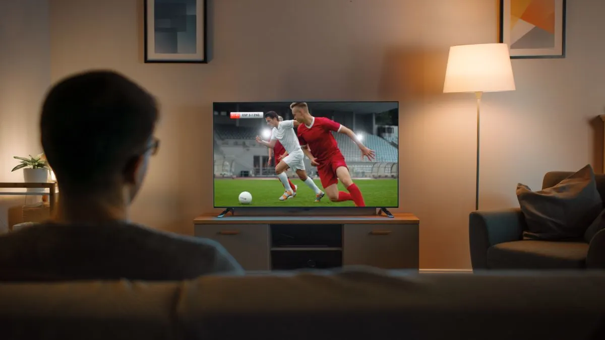 Ein Mann sitzt auf einem Sofa und sieht ein Fußballspiel auf einem Fernseher.