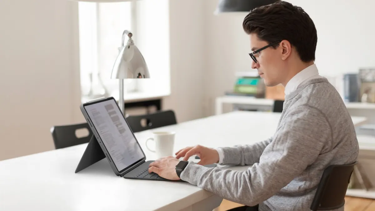 Ein Mann sitzt an einem Tisch und tippt auf der Tastatur der iPad-Hülle Logitech Combo Touch.