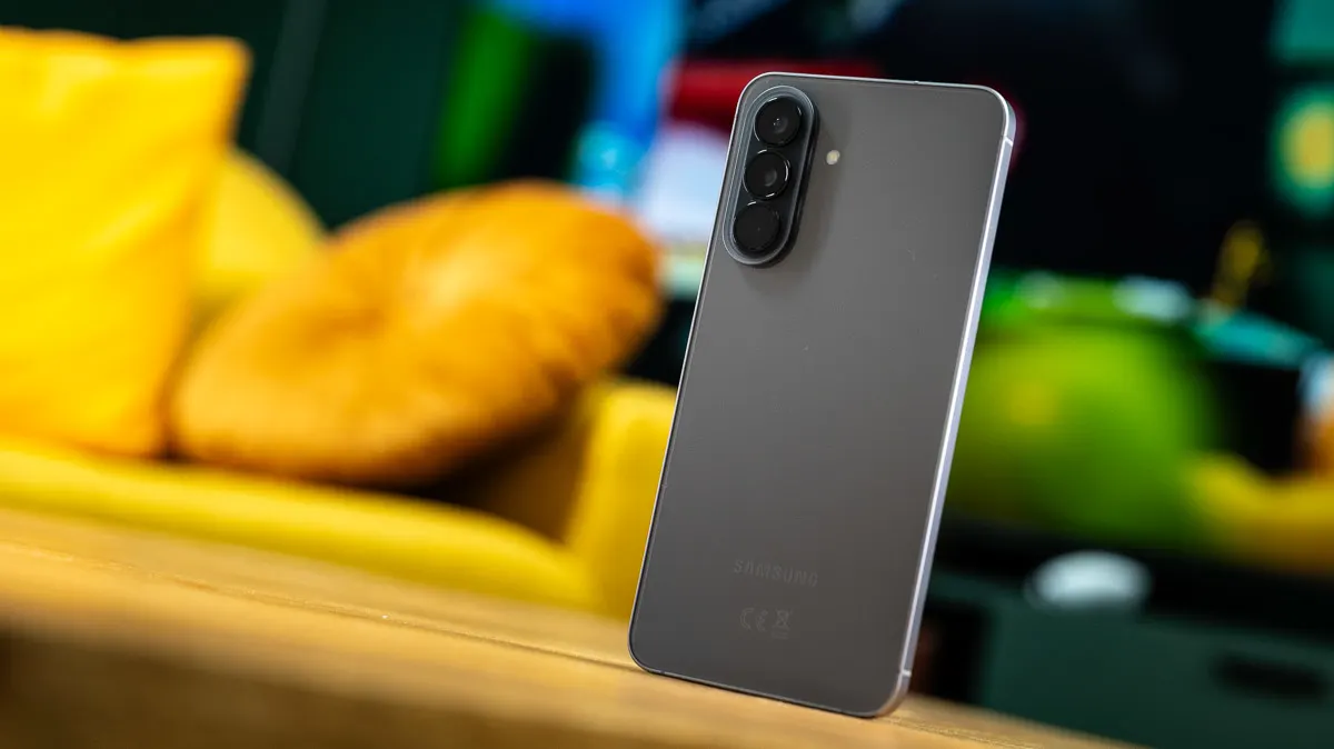 Das Samsung Galaxy A57 steht mit der Rückseite zur Kamera auf einem Sofatisch. Im Hintergrund steht ein gelbes Sofa.