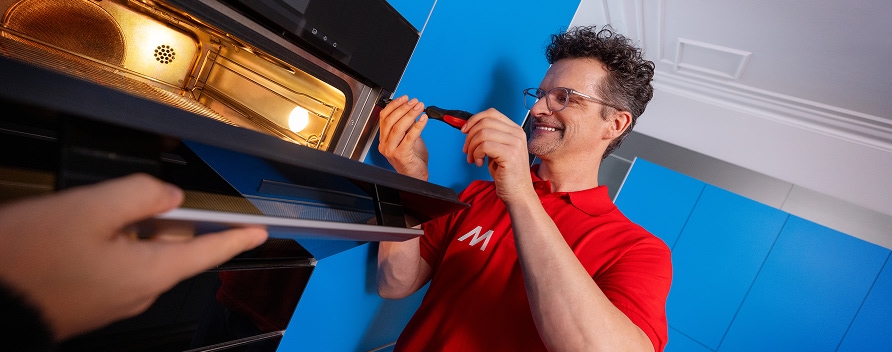 Techniker schließt mit Werkzeug einen Einbau-Backofen Herd direkt in der Küchenzeile an.