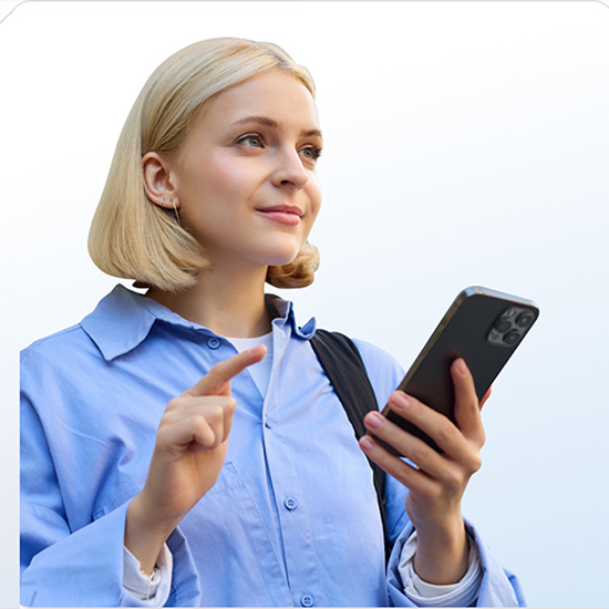 Junge Dame mit blondem Bob in hellblauem Hemd hält Smartphone und tippt; Schultergurt sichtbar, neutraler Hintergrund.