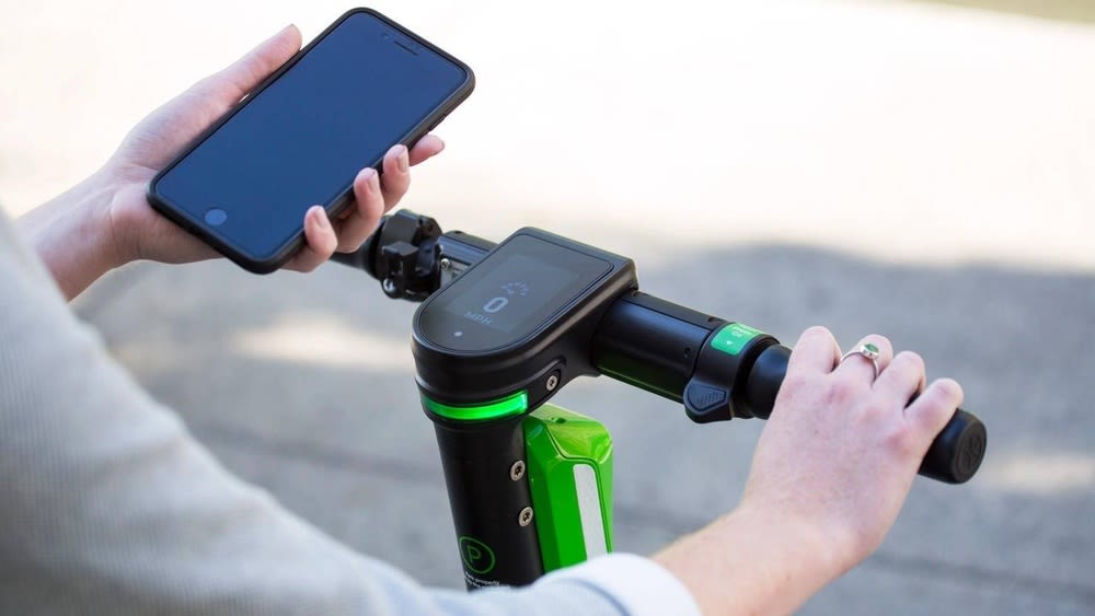 Frau hält iPhone neben grün-schwarzen E-Scooter