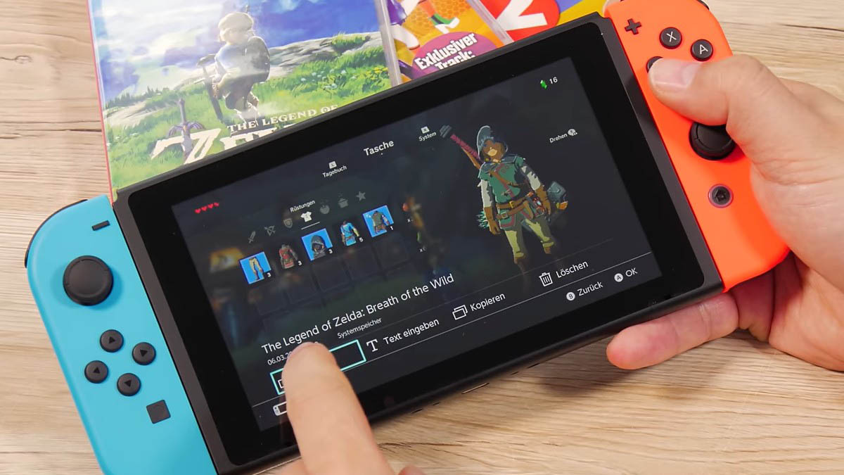 Eine Person hält eine Nintendo Switch mit blauem und rotem Controller, auf dem "The Legend of Zelda" läuft. 