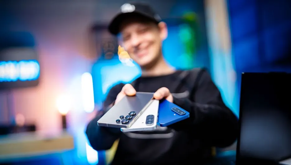 Alex lächelt und hält drei Samsung-Smartphones wie einen Fächer in die Kamera.