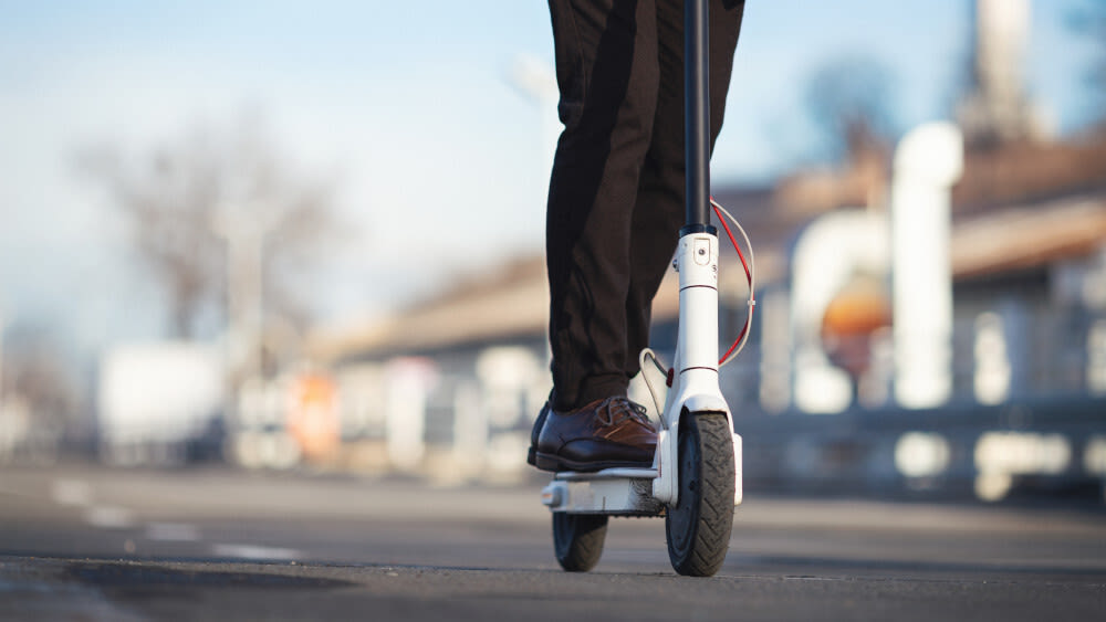 Mann mit braunen Hosen und Schuhen fährt auf weißem E-Scooter