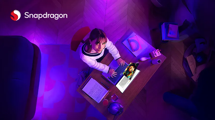 Eine Person sitzt an einem Tisch und benutzt einen Laptop. Bücher und Notizen liegen auf dem Tisch. Das Snapdragon-Logo ist sichtbar.