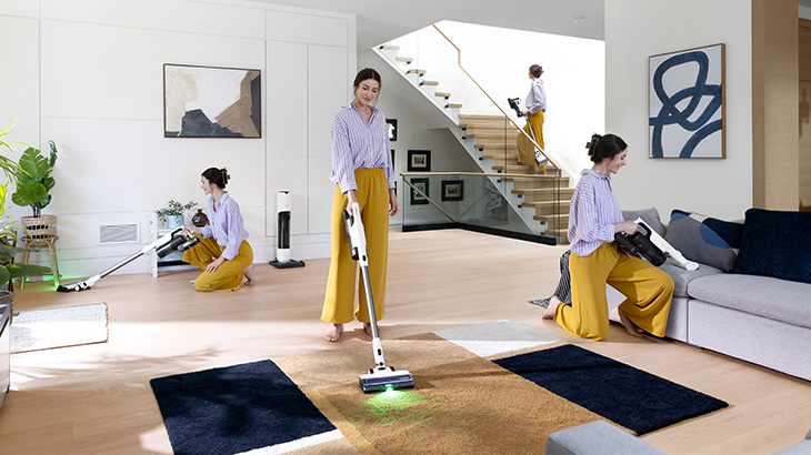 Ein Wohnzimmer mit Holzfußboden, beigem Sofa und Teppich. Eine Person putzt mit einem Staubsauger Möbel und Böden.