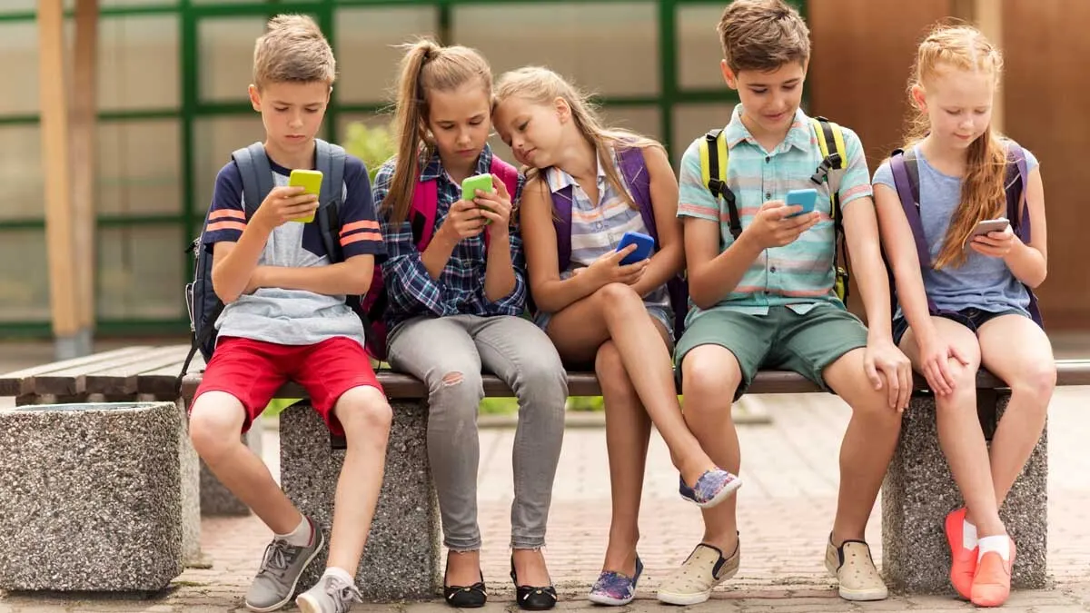 Eine Gruppe von Kindern sitzt auf einer Bank und schaut aufs Handy.
