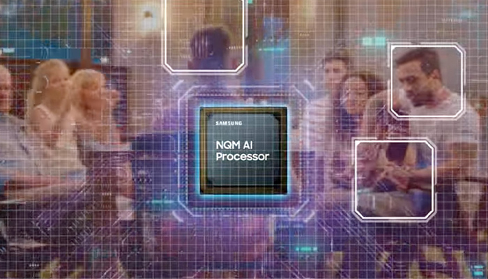Eine Gruppe von Menschen steht vor einem Hintergrund mit einem blauen Gittermuster. Ein NQM AI Prozessor von Samsung ist im Vordergrund zu sehen.
