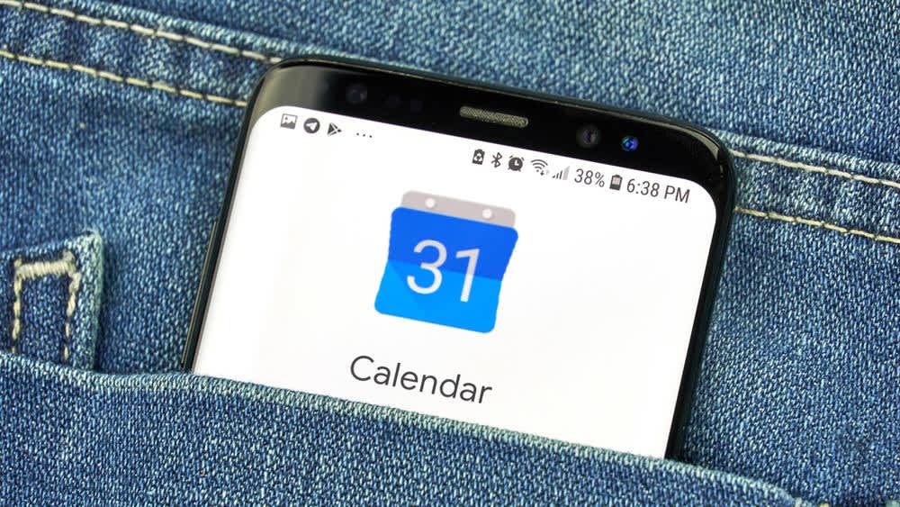 Ein Smartphone mit einer Kalender-App auf dem Display schaut aus einer Hosentasche heraus.