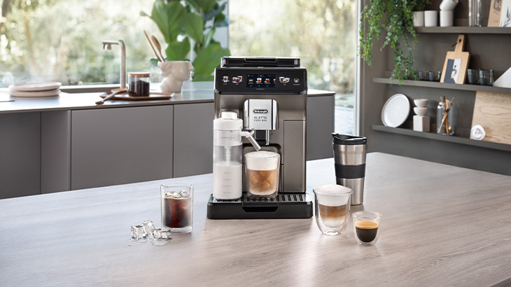 Kaffeemaschine auf einer Küchentheke mit Tassen, Kaffeebohnen und einer Papiertüte vor einem Fenster.