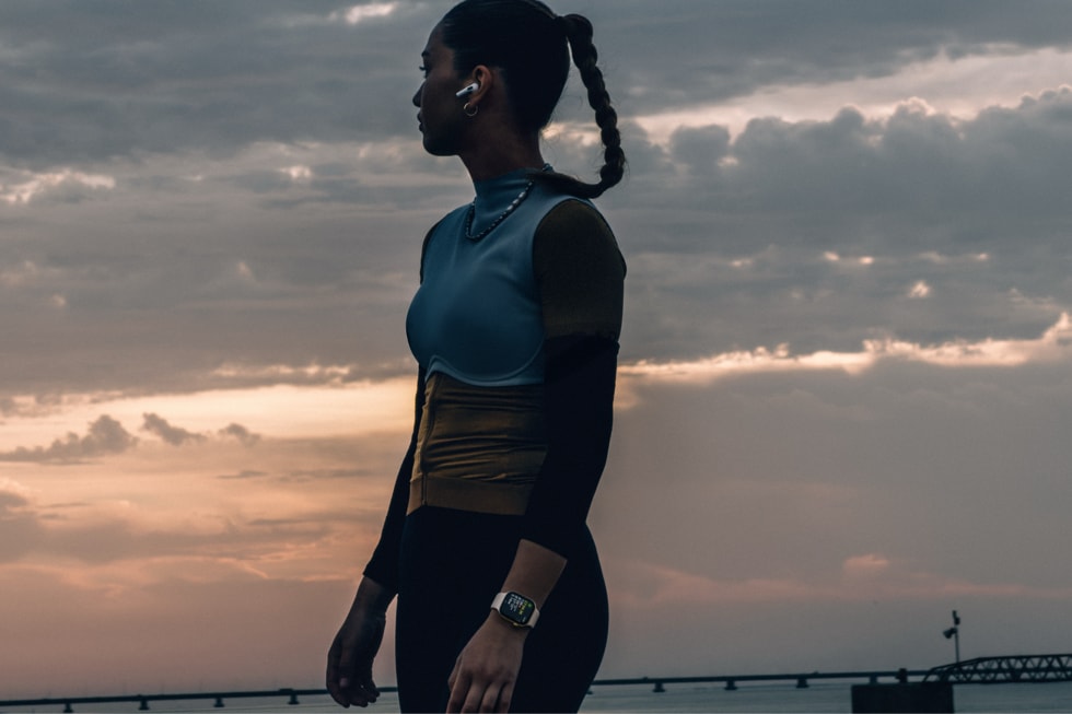 Eine Frau steht in Sportkleidung am Meer und trägt die Apple Watch Series 12 am Handgelenk.