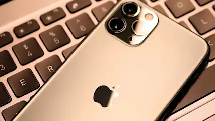 Ein Smartphone mit drei Kameras und Apple-Logo liegt auf einer Computertastatur mit schwarzen Tasten.