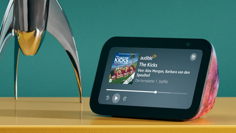 Der Amazon Echo Show 5 Kids steht neben einer Raketenlampe und spielt ein Audible-Hörbuch ab.