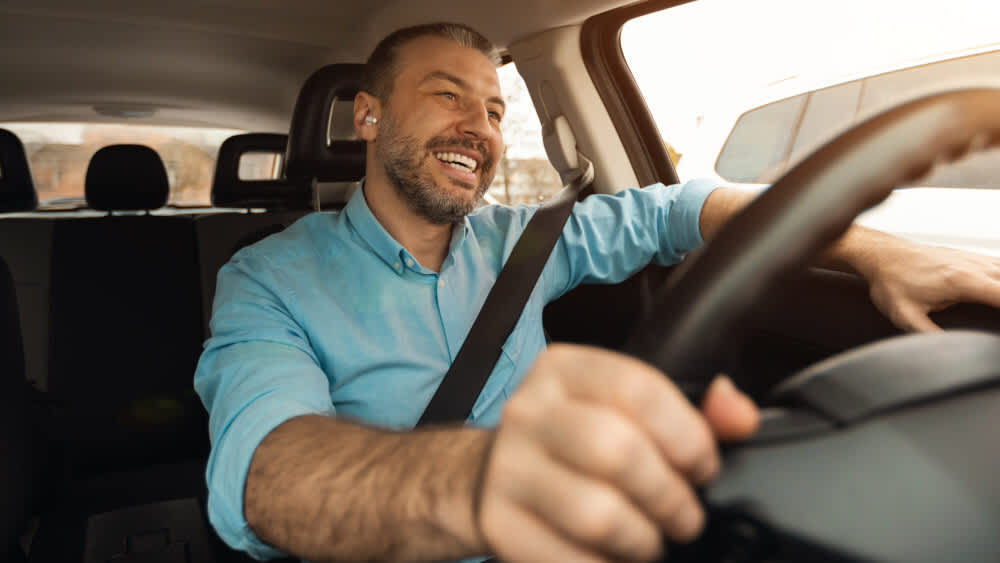 Ein Mann sitzt am Steuer eines Autos und lächelt.