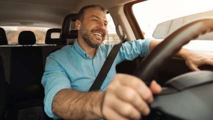 Ein Mann sitzt am Steuer eines Autos und lächelt.