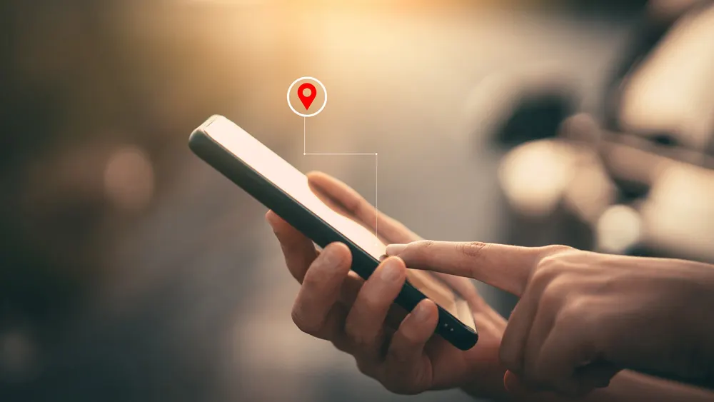Eine Person tippt mit dem Finger auf das Display eines Smartphones, darüber erscheint das Standortsymbol.