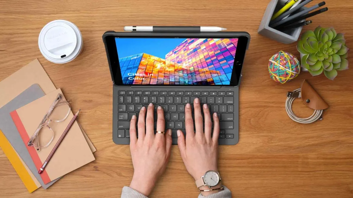 Eine Person tippt an einem Tisch auf der Tastatur der iPad-Hülle Logitech Slim Folio.