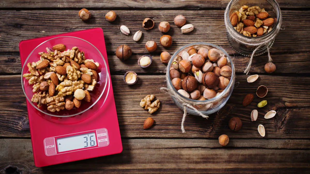 Auf einer pinken Küchenwaage steht eine Schüssel mit Nüssen. Daneben Gläser mit noch mehr Nüssen.